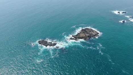 Vista-Aérea-De-Las-Islas-Rocosas-Bañadas-Por-Las-Tranquilas-Olas-Del-Océano-En-La-Costa-De-Java-Indonesia