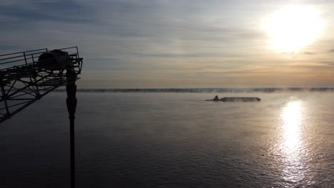 Luftaufnahme-Von-Der-Drohne,-Das-Boot-Segelt-Morgens-Auf-Dem-Fluss,-Der-Nebel-Und-Die-Sonne-Runden-Das-Bild-Ab