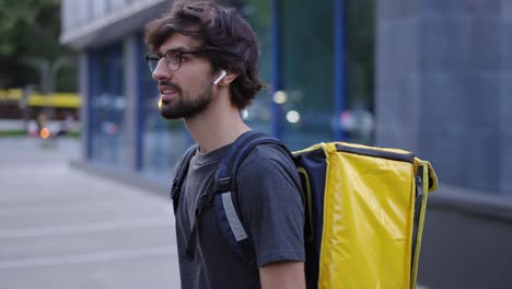 hombre de entrega caminando con bicicleta y bolsa amarilla por la ciudad moderna