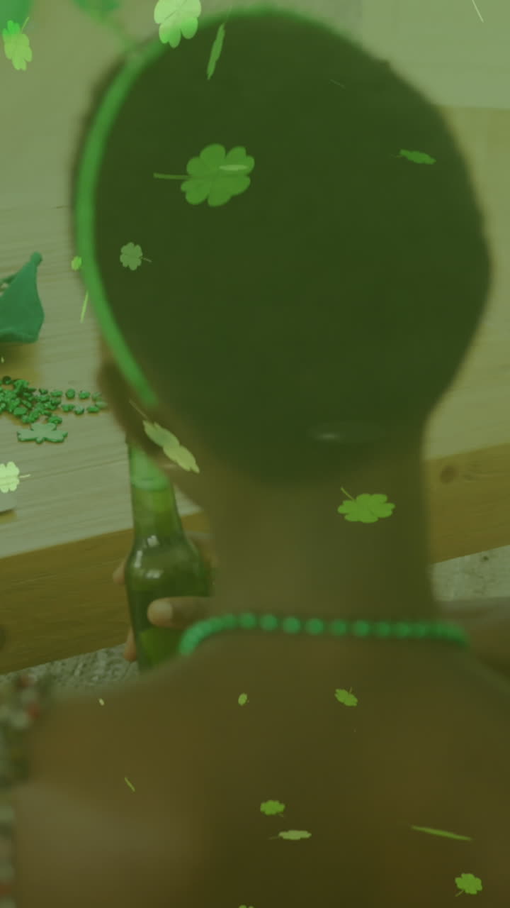 hojas de trébol que caen contra una pareja sosteniendo cervezas haciendo una videollamada en una computadora portátil en casa