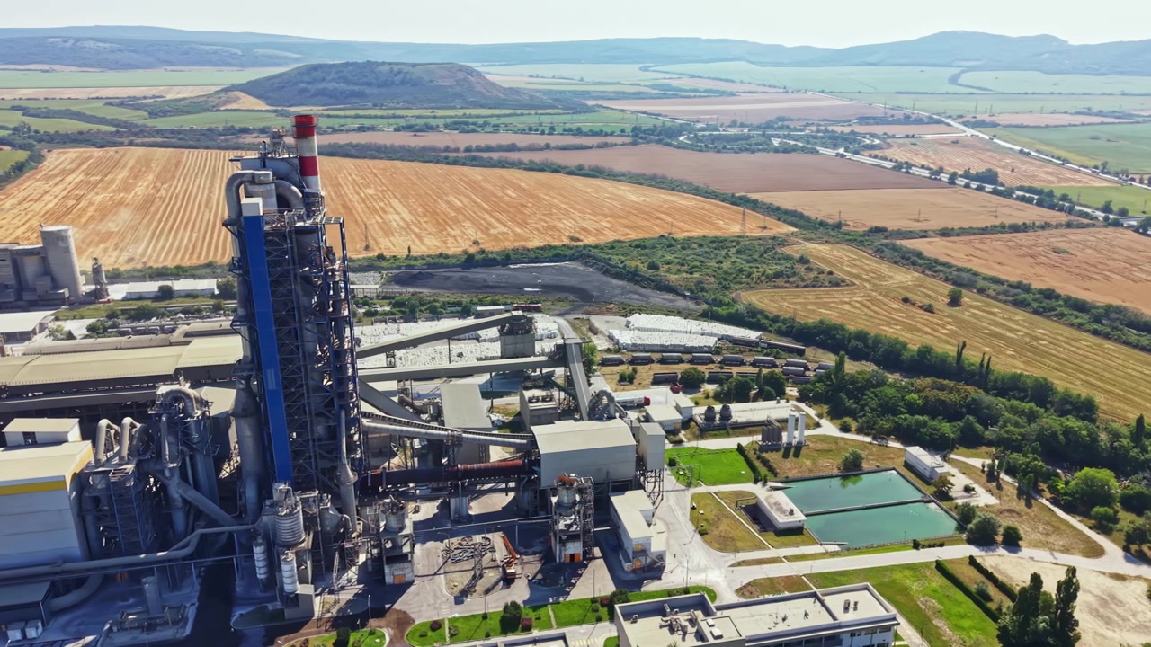 Impianto industriale situato in una zona rurale con terreni agricoli e colline sullo sfondo, scattata durante il giorno.