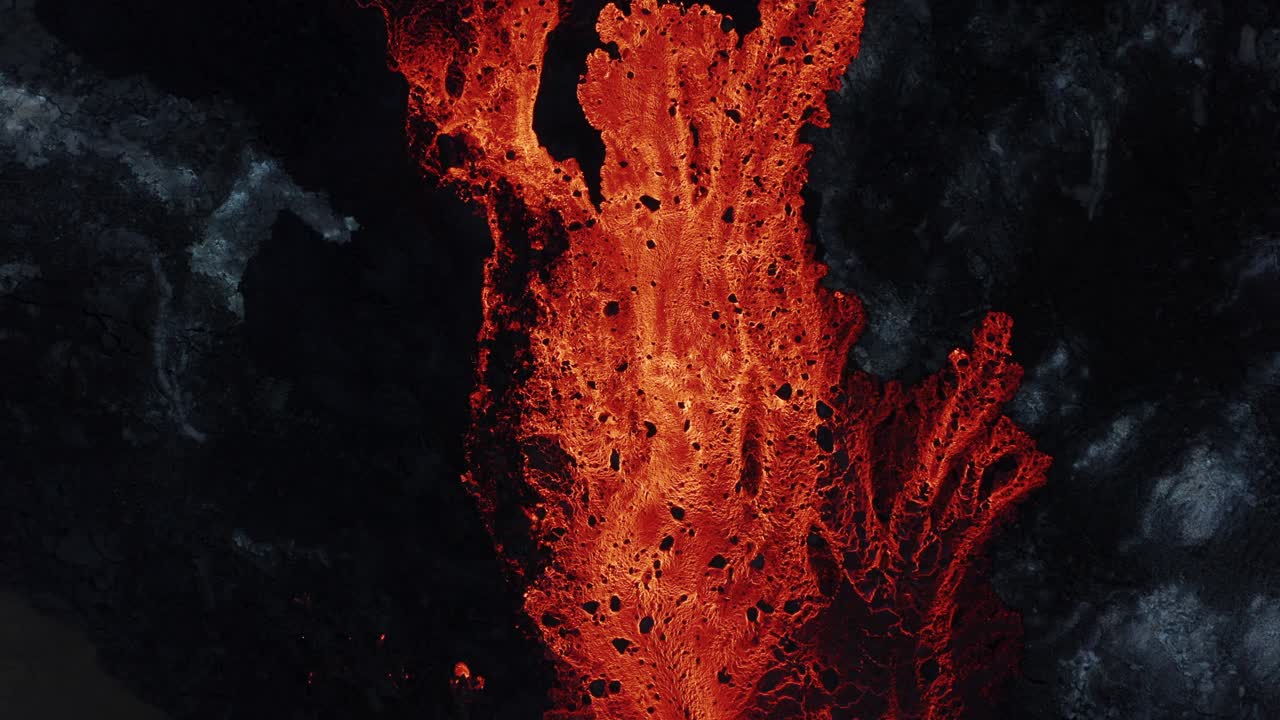 Large flowing river of molten red lava in rugged volcanic environment, top down