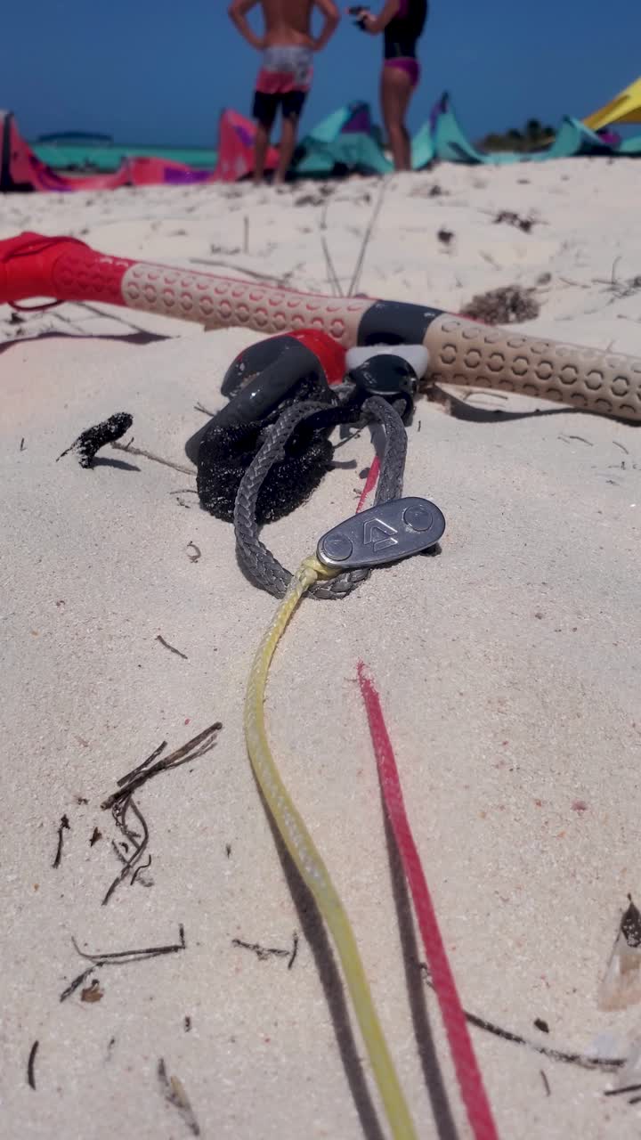 Footage showcases kite surfing gear on a sandy beach, with two individuals engaging in conversation nearby, surrounded by colorful kites and clear blue skies.