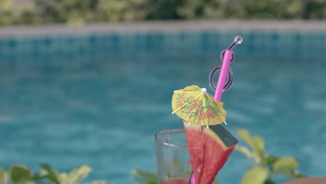 glass with straws and drink umbrella stands against pool