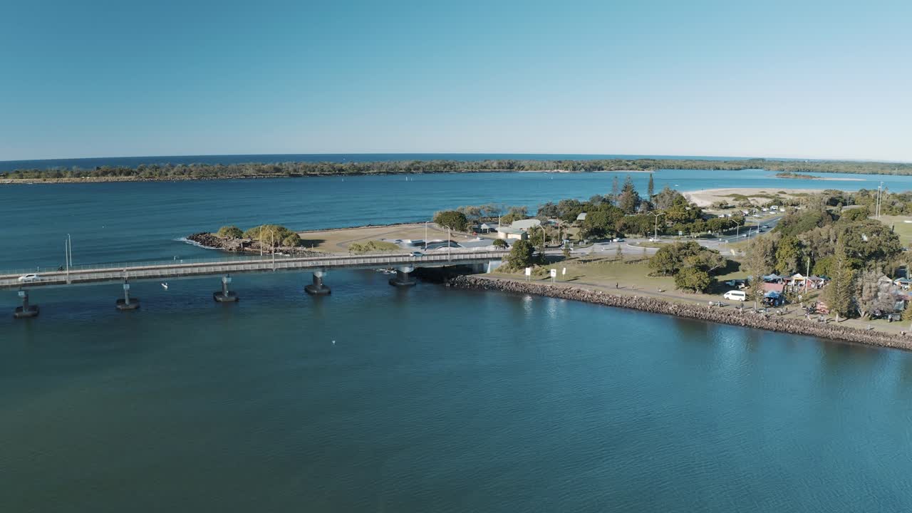 Aerial view of a scenic bridge crossing over calm coastal waters, with surrounding greenery and open skies, showcasing the peaceful and natural beauty of the landscape