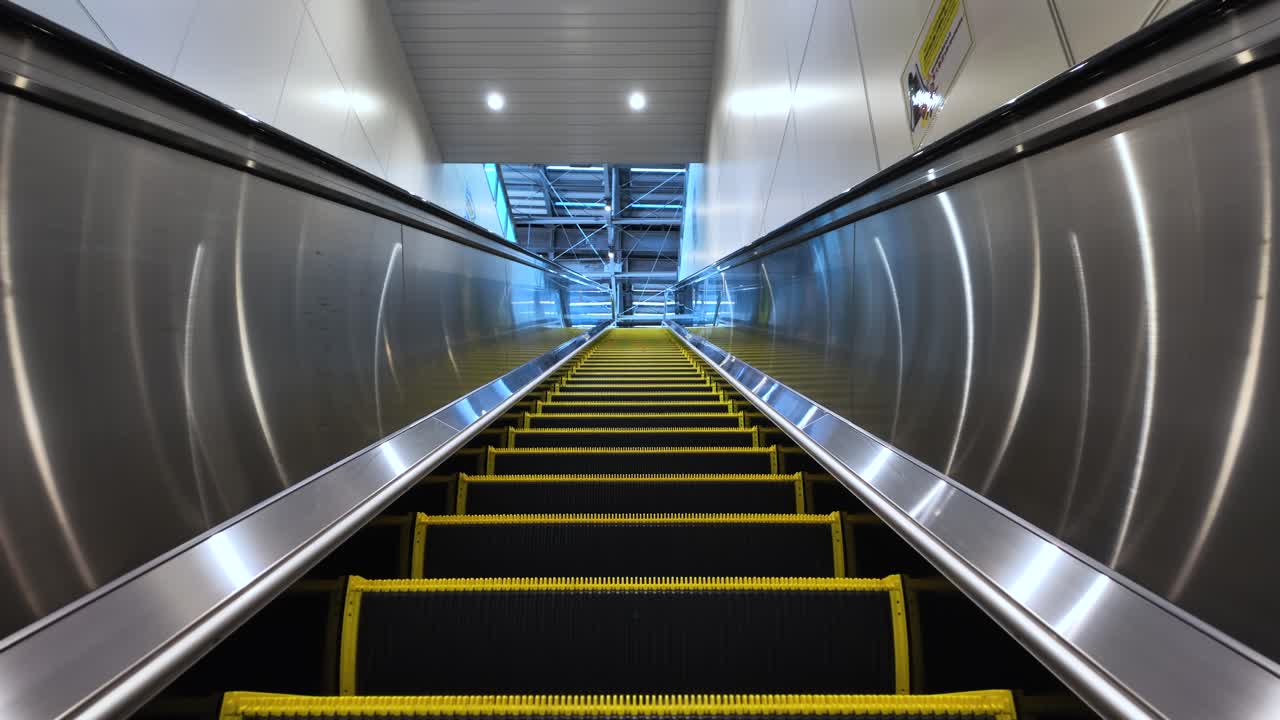 POV of an empty escalator going up in a modern building with metal side walls