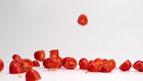 fresh, bright red halved cherry tomato fruits and vegetables landing down and bouncing on white table top in slow motion