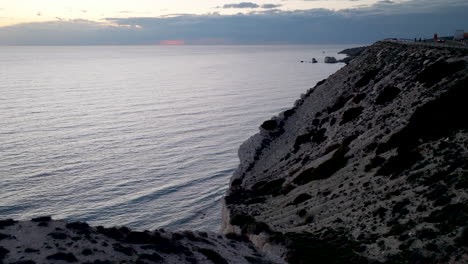 Paisaje-Marino-Oscuro-A-Lo-Largo-De-La-Costa-De-Chipre,-Donde-La-Carretera-Junto-Al-Acantilado-Abraza-El-Terreno-Accidentado-Con-Vistas-Al-Tranquilo-Mar-Mediterráneo-Al-Atardecer