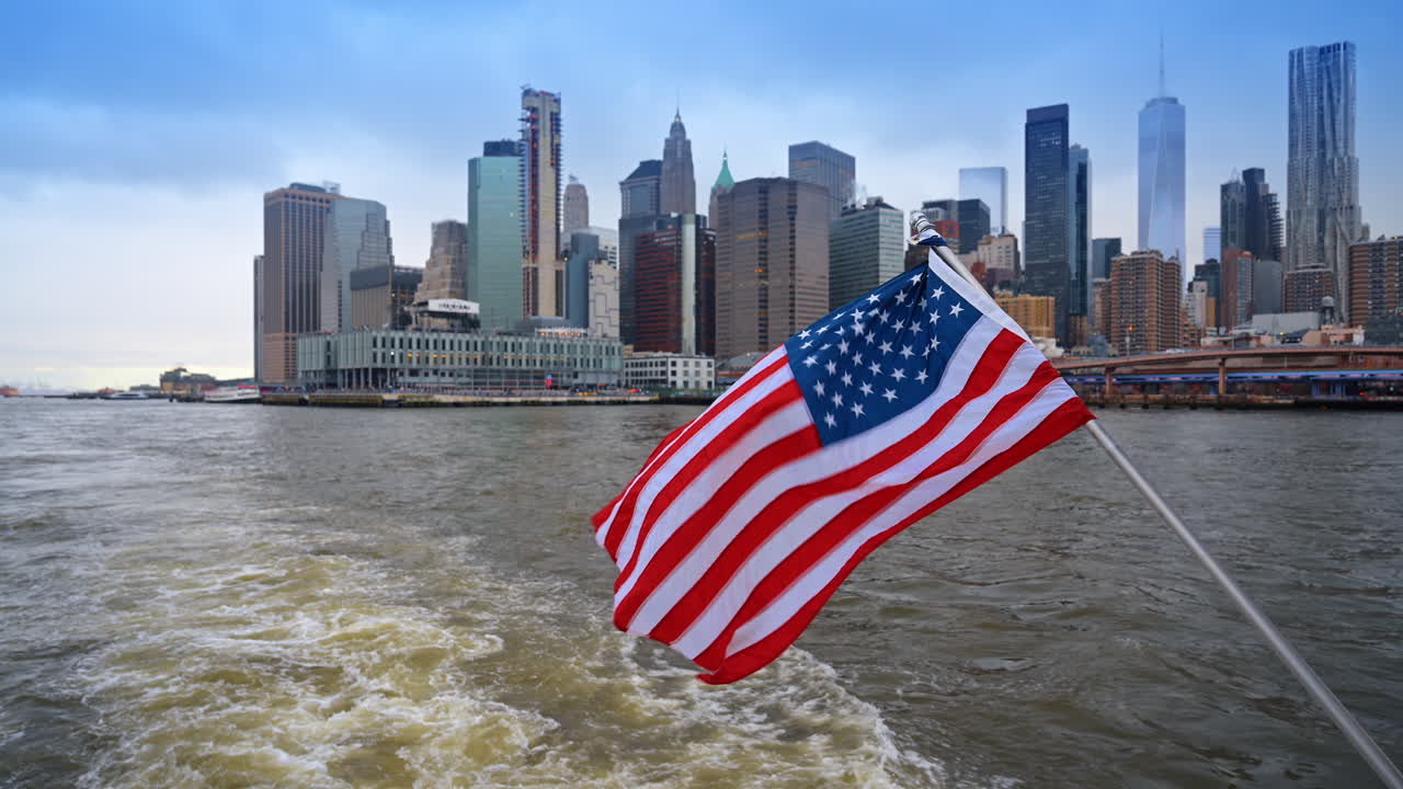 Bandiera americana che sventola con lo skyline di Lower Manhattan sullo sfondo. Bandiera degli Stati Uniti su una barca con vista sul One World Trade Center e grattacieli sull'acqua.