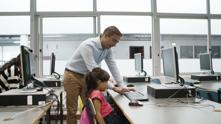Ein Lehrer steht neben einem Mädchen und hilft ihr bei der Computerarbeit.