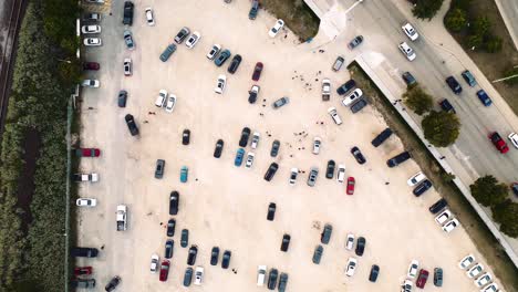 un dron cinematográfico de rastreo creativo de arriba hacia abajo de 4k de largo toma una toma aérea de pequeñas personas hormigas control de multitudes dejando el parque shaw en winnipeg manitoba caminando por un estacionamiento de tierra de grava coches coloridos