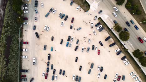 a top down creative tracking cinematic drone 4k long take aerial shot of small people ants crowd control leaving shaw park in winnipeg manitoba walking on a gravel dirt parking lot colorful cars