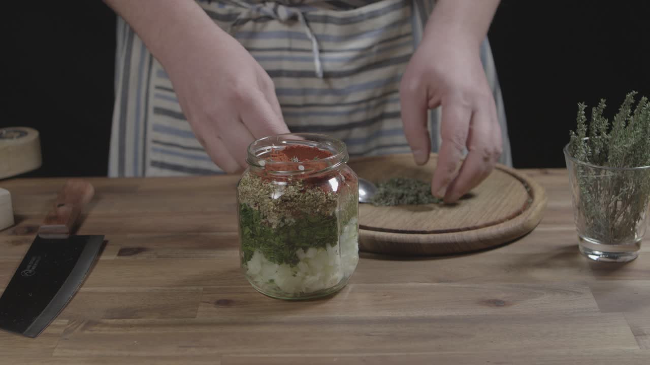 Adding spices to jar for chimichurri preparation with a spoon, chef makes sauce for argentine barbecue