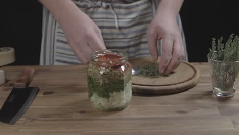 adding spices to jar for chimichurri preparation with a spoon, chef makes sauce for argentine barbecue