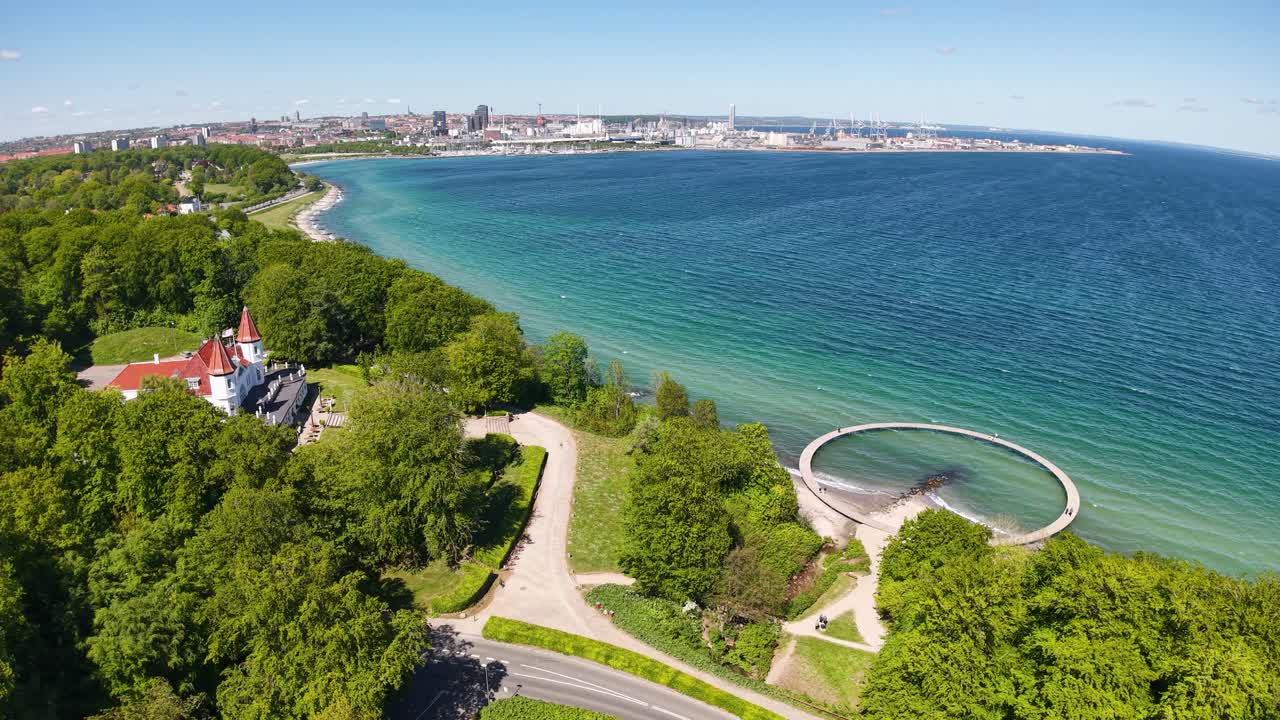 Aerial view of Infinite Bridge on Aarhus Bay with clear shoreline, green trees, and blue water