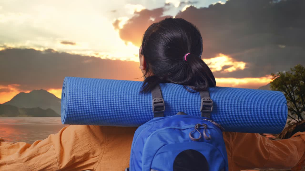 Close Up Back View Of A Female Hiker With Mountaineering Backpack Spreading Arms And Looking The View Around While Standing At A Lake During Sunset Time