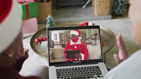 Diverse-senior-female-friends-using-laptop-for-christmas-video-call-with-santa-on-screen