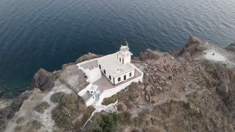 Aerial-view-of-the-famous-Akrotiri-lighthouse-on-top-of-rocky-mountain-during-a-beatiful-sunset-in-Santorini,-Greece