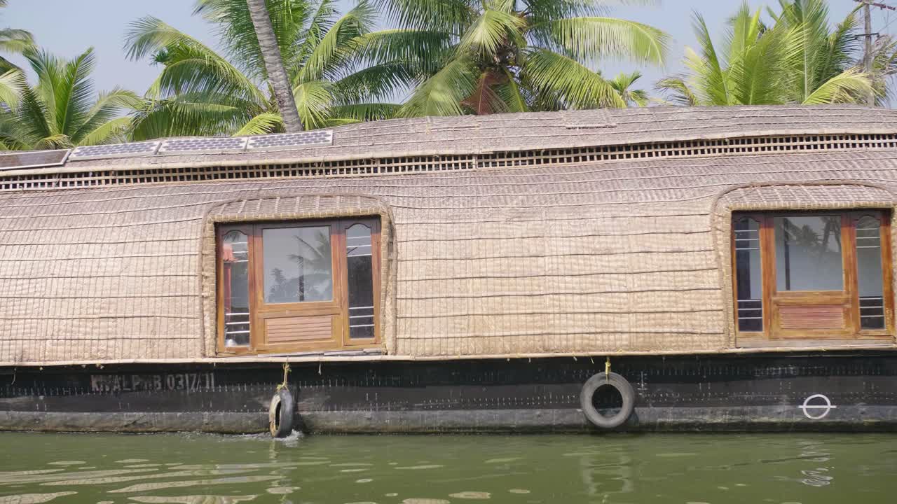 una casa flotante elegante y tradicional flota en el sitio del patrimonio de los remansos de kerala con palmeras en el fondo durante el calor del día