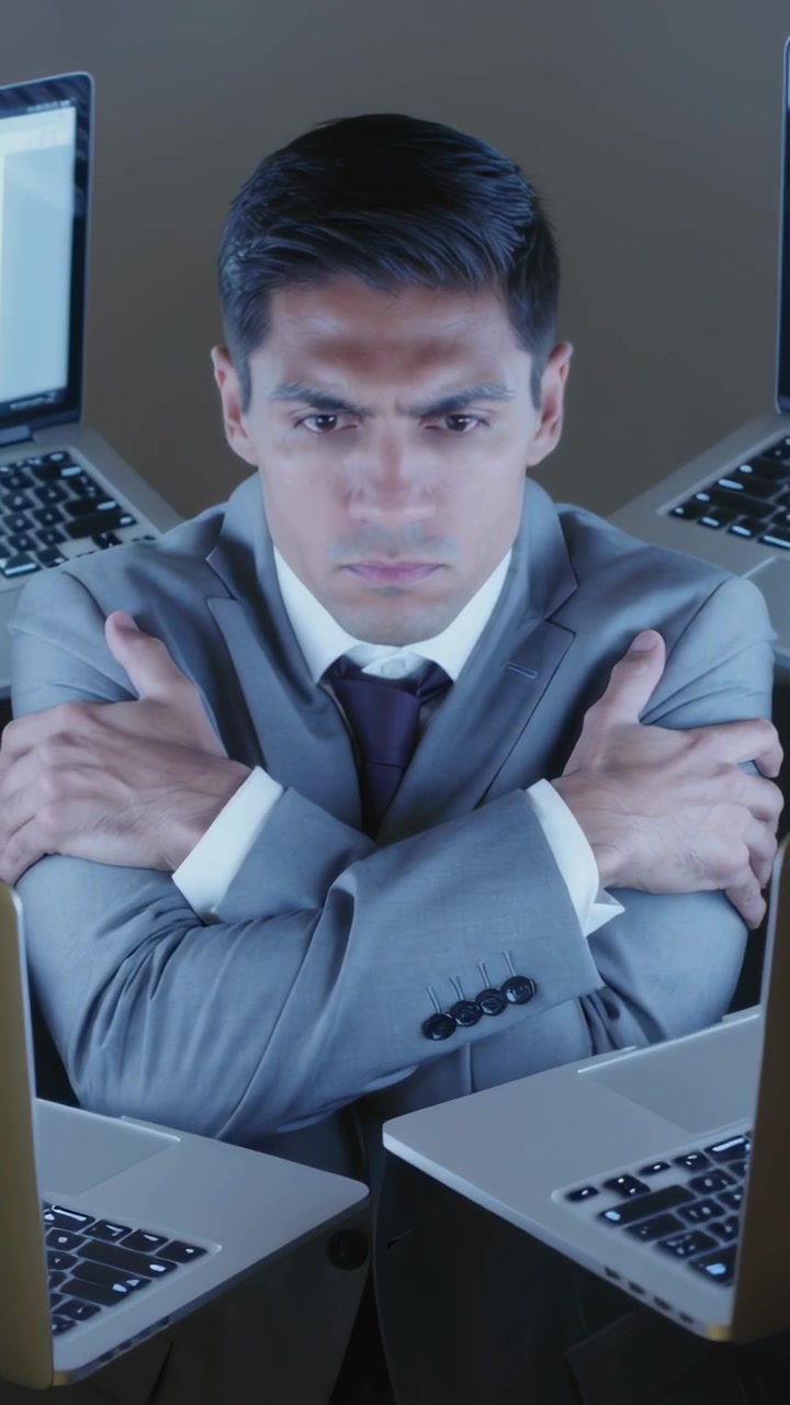 Video verticale: Uomo seduto in abito che incrocia le braccia in ufficio, con i laptop che si muovono per proteggere la privacy