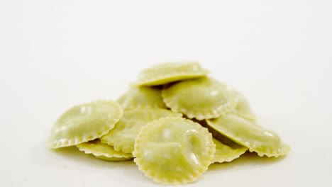 stack of green homemade ravioli pasta on white background