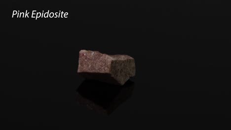 un mineral de epidosita rosado que gira sobre un fondo negro