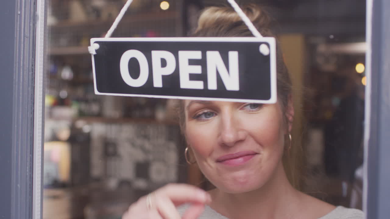 propietaria de una pequeña empresa girando un letrero abierto en una tienda o cafetería