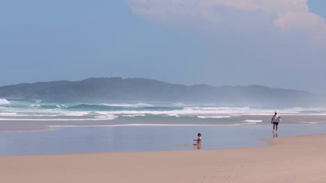 a serene beach scene with two people walking along the shore, distant hills in the background.