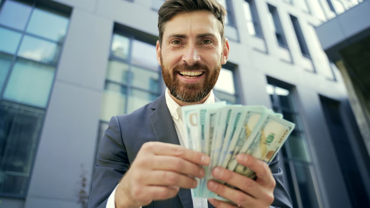 Uomo d'affari caucasico barbuto, felice e di successo, conta, sventola, lancia e ostenta denaro contante su sfondo.