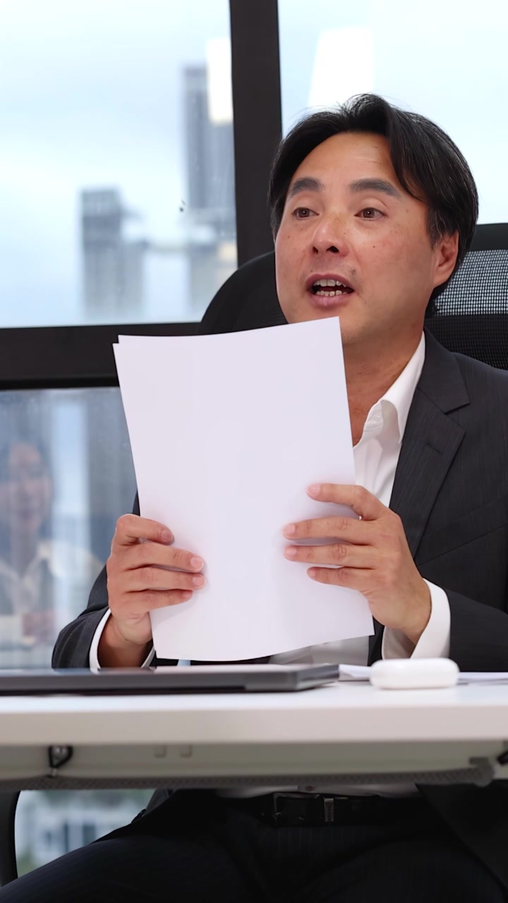 Mezza figura di un uomo d'affari asiatico in abito che legge documenti durante una riunione d'ufficio.