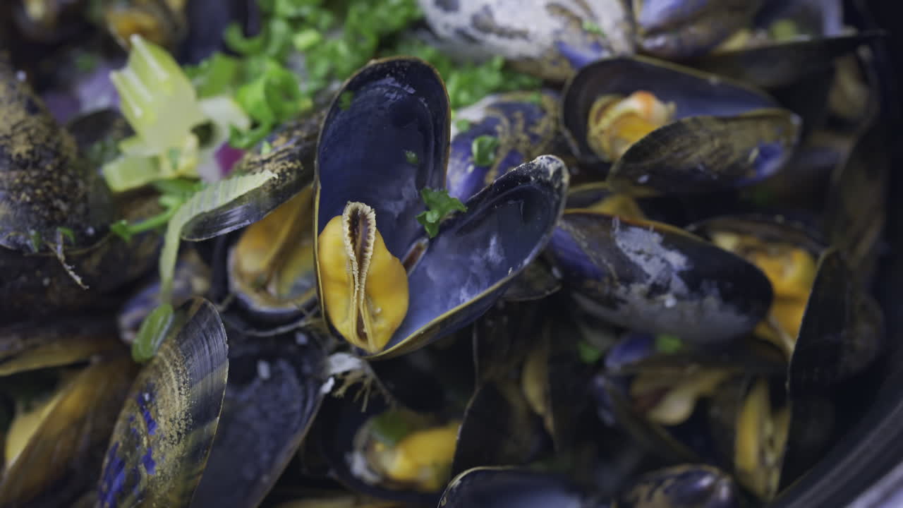 Close up of multiple steamy mussels in a pot with green onions on top