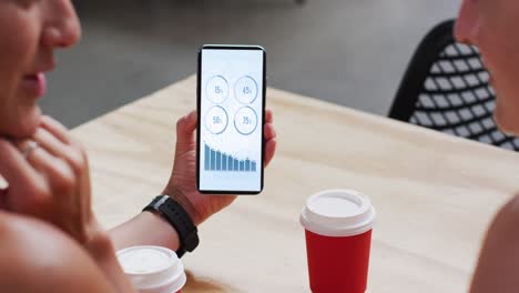 caucasian man and woman sitting at table, using smartphone with statistics on screen