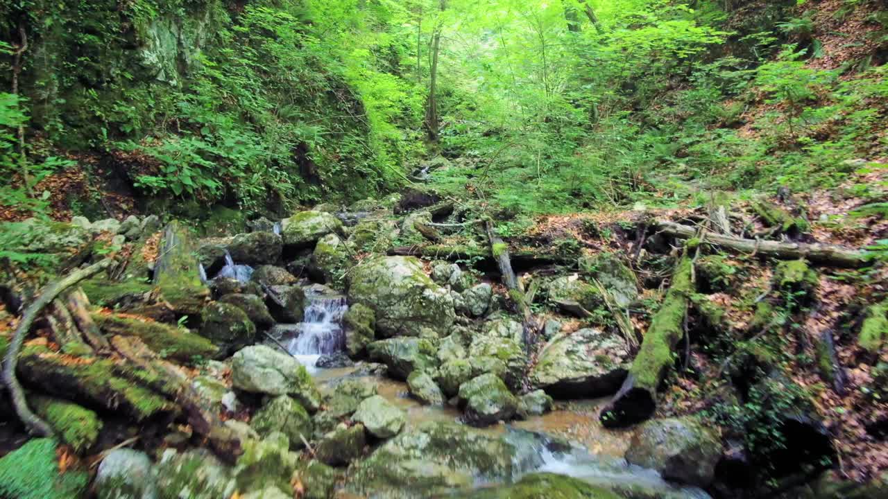 Aerial: Flying forward slightly above slippery rocky terrain with a small stream surrounded with lush forest and hills