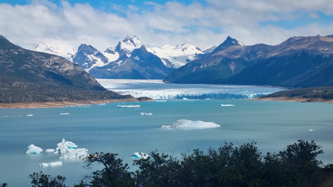 Panoramica sul Lago Argentino con iceberg galleggianti, incorniciato dalle cime innevate delle Ande e dall'iconico Ghiacciaio Perito Moreno, in una giornata calma e parzialmente nuvolosa in Patagonia.