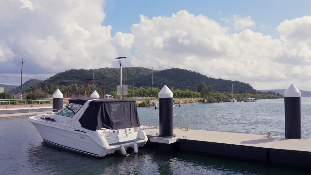 Motoscafo ormeggiato accanto a un pontile galleggiante con acqua calma e colline sullo sfondo, Woy Woy, Nuovo Galles del Sud, Australia