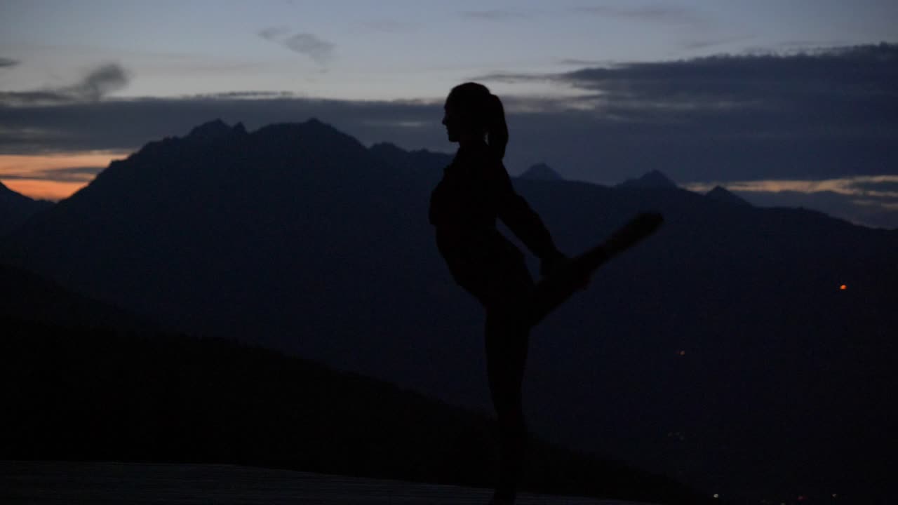Slow motion: Beautiful shot of silhouette of a young woman dancing and doing Natarajasana on a plattform at dusk