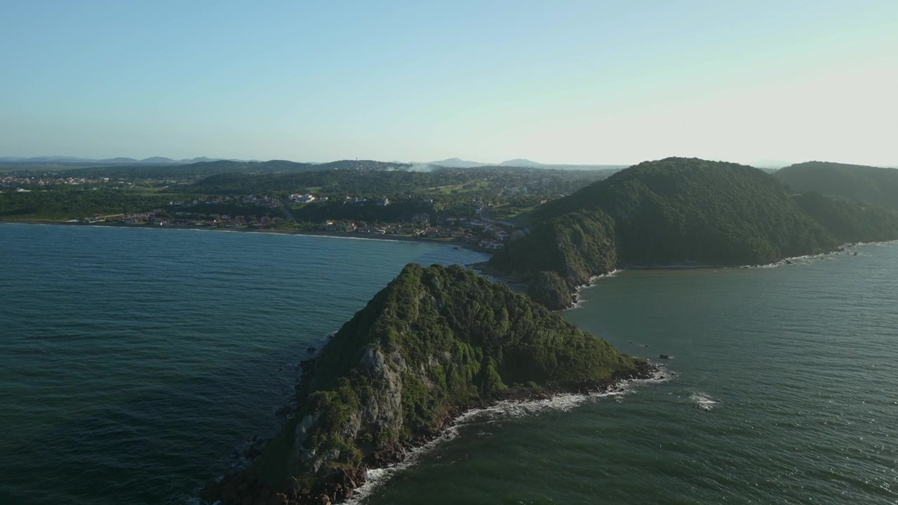 Mirante do Pai e Praia da Marina in una luminosa mattina di sole. Avvicinamento aereo che si libra sulle acque blu verso una piccola isola rocciosa e una spiaggia. Ripreso in 4K a 25 fps