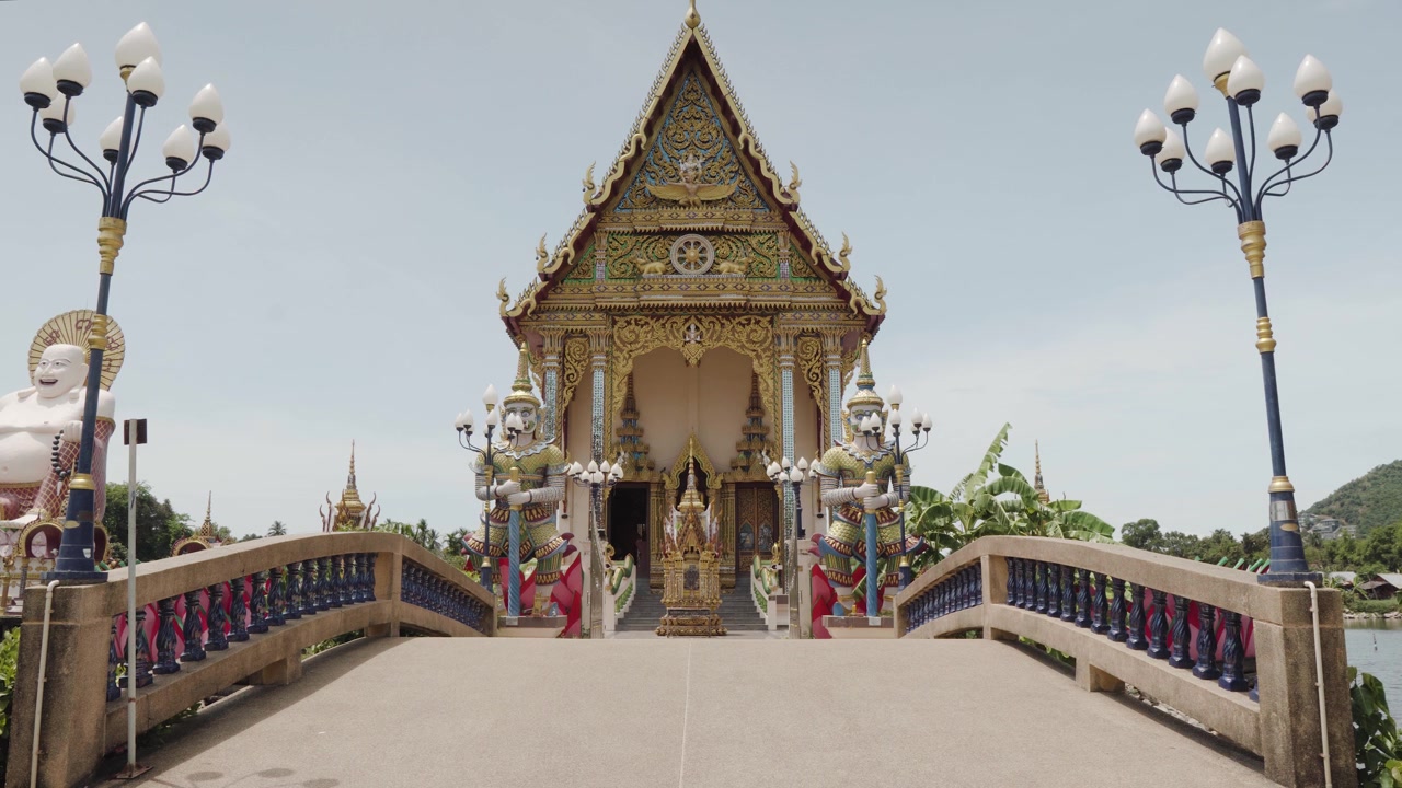 Inquadratura statica del tempio Wat Plai Laem dietro il ponte in una giornata di sole, con palme che ondeggiano al vento