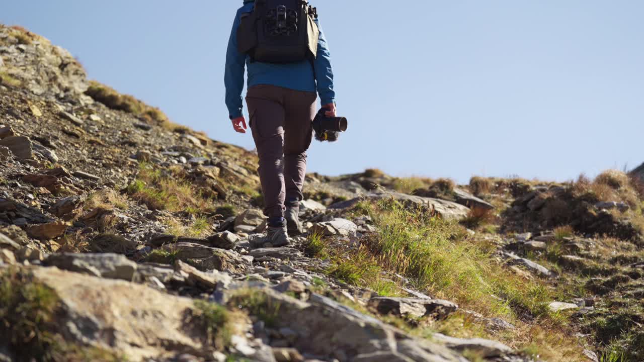creador de contenido de senderismo en solitario con cámara caminando por la ladera de una montaña rocosa