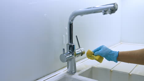 cleaning a modern faucet. a person is scrubbing a shiny kitchen faucet to remove dirt and grime while wearing blue gloves