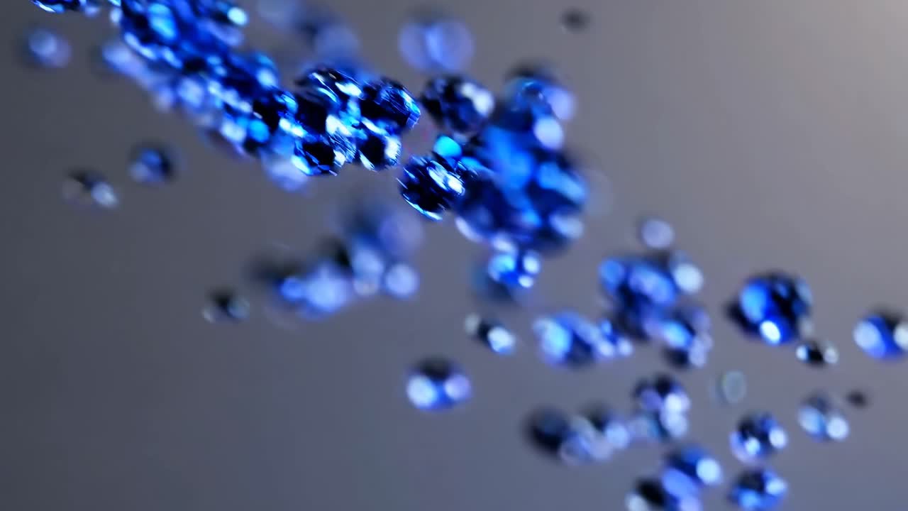 Close-up video of blue liquid droplets suspended in mid-air, captured with a shallow depth of field