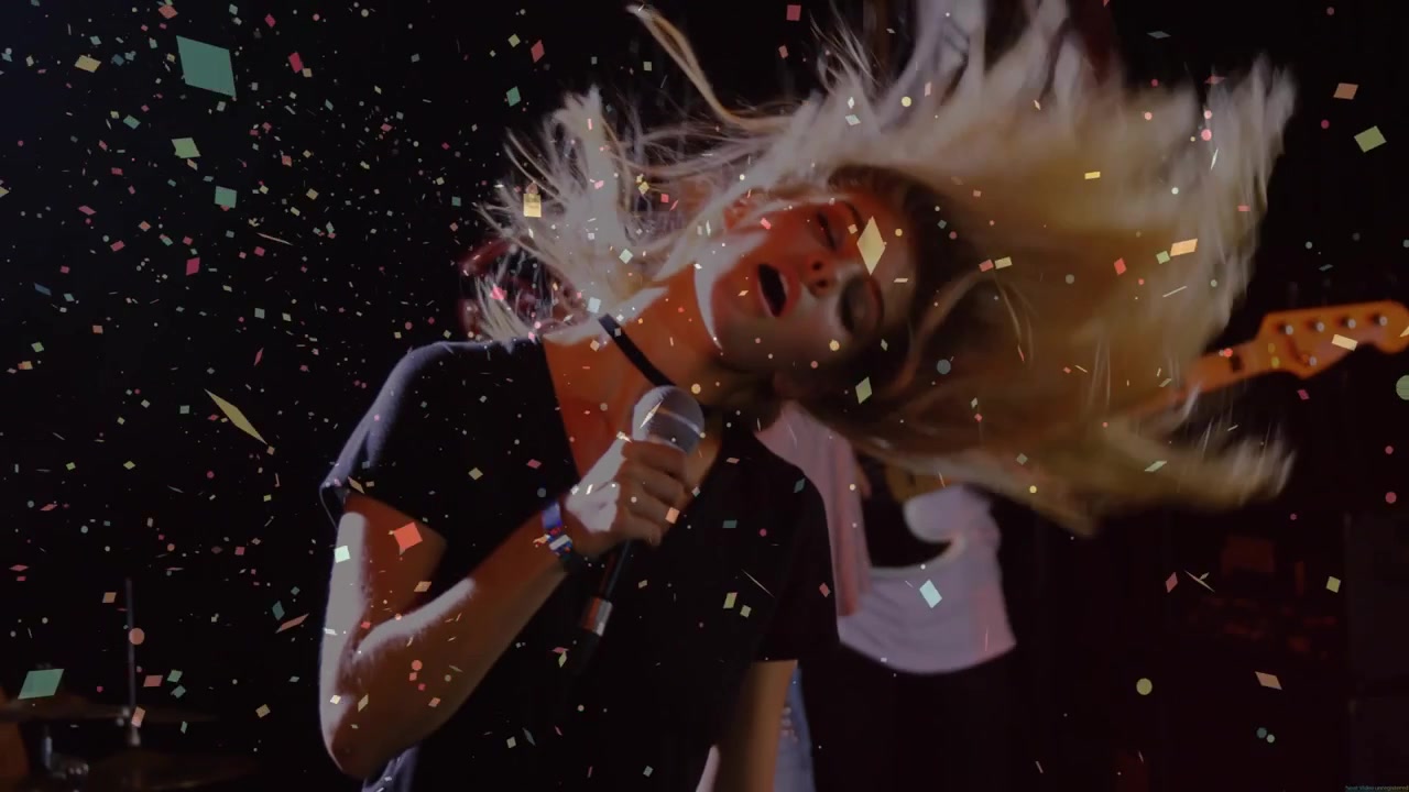 Vertical video: Camera pulling back, lead singer in shorts, crop top, singing mic, confetti falling