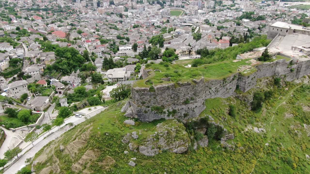 알바니아 의 드론 전망 은 gjirokaster 마을 에서 비행 하는 중세 성 위 에 있는 높은 지상 의 요새 에 있는 벽돌 갈색 지붕 집 들 을 보여 준다