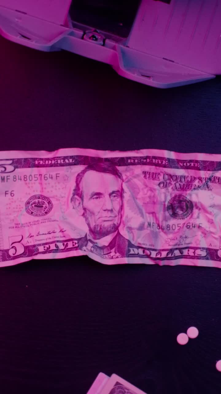 Banconota da cinque dollari e pillole sotto luce rosa