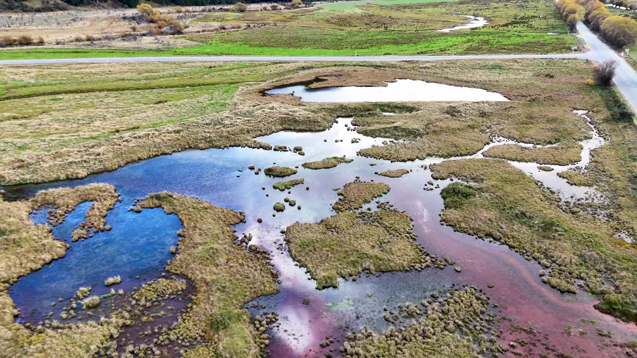 Aerial footage captures colorful wetlands with vivid blue and purple hues under natural light in Glenorchy, New Zealand