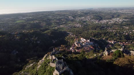 cinematic drone shot flying above ruins of castelo dos mouros and slowly revealing old town of sintra and vastness of landscape, lisbon, portugal