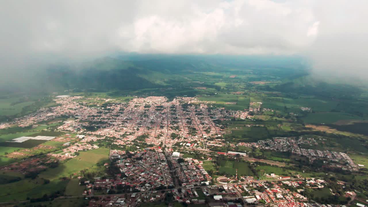 Reveal shot of small Mexican town with grid like street layout surrounded by lush farmland and distant mountains, Tuxpan, Mexico. Slow motion drone aerial