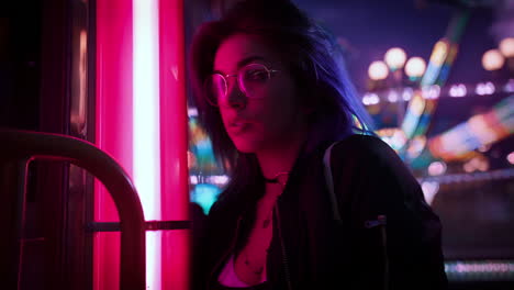 cinemagraph of thoughtful caucasian teenage girl in glasses at funfair with flashing lights at night