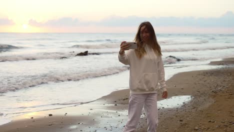 beautiful young woman spinning around on ocean beach at sunset, filming herself with her phone