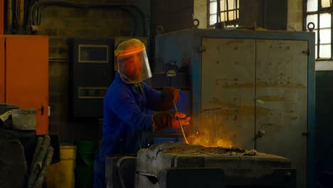 Male-worker-mixing-molted-metal-in-container-at-workshop-4k